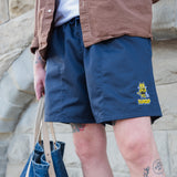 Person wearing navy shorts with a logo, standing against a stone wall.
